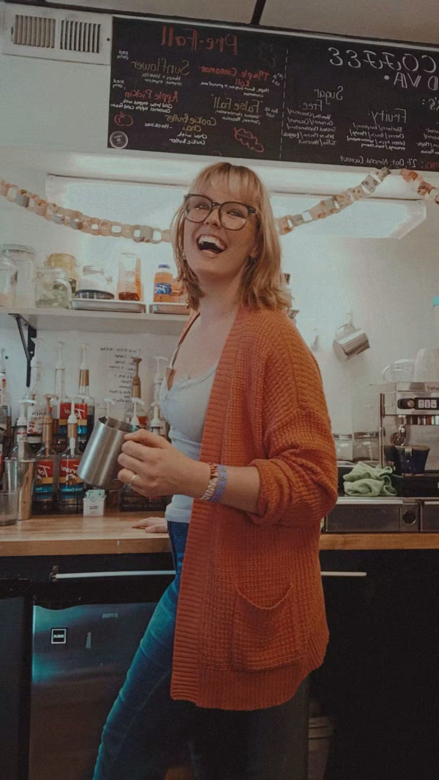 Smiling person holding a milk pitcher at the First XI café counter